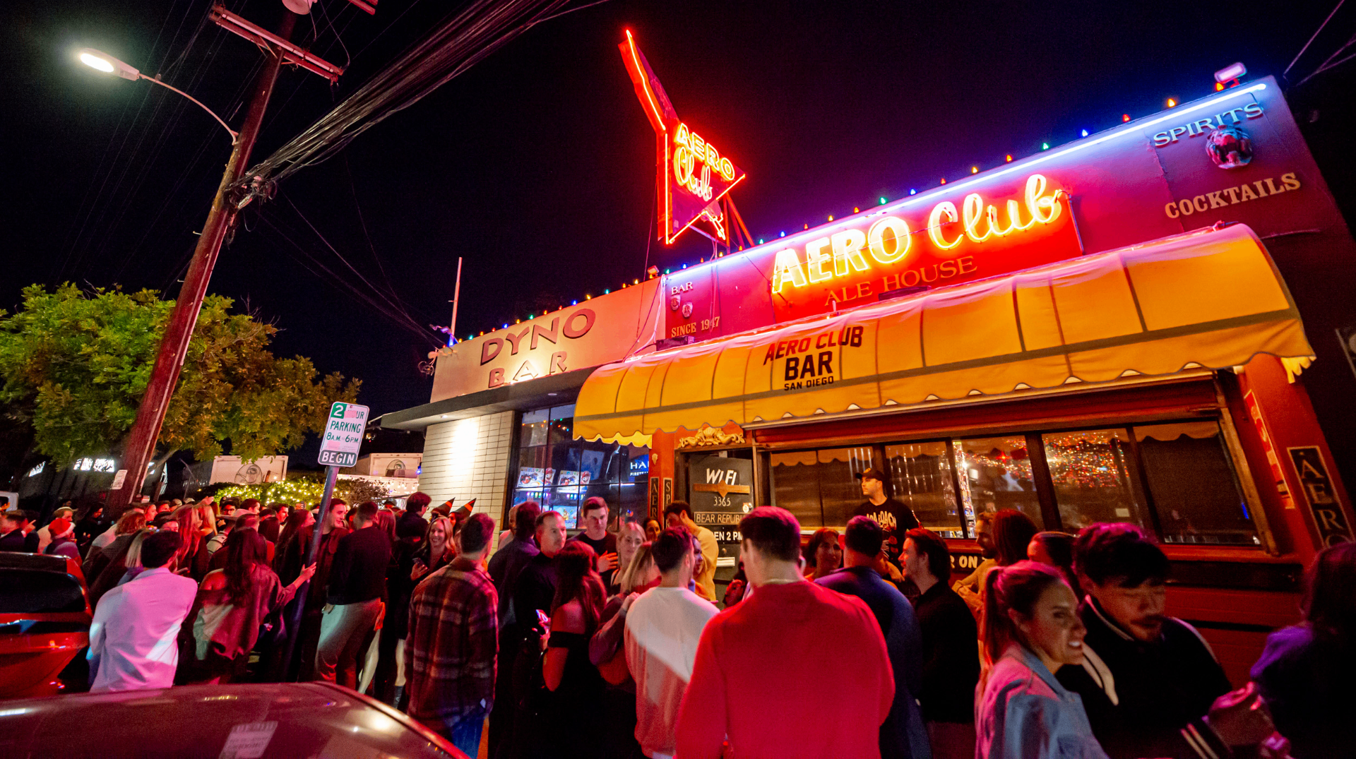 Aero Club Bar exterior at night with neon signs and a crowd
